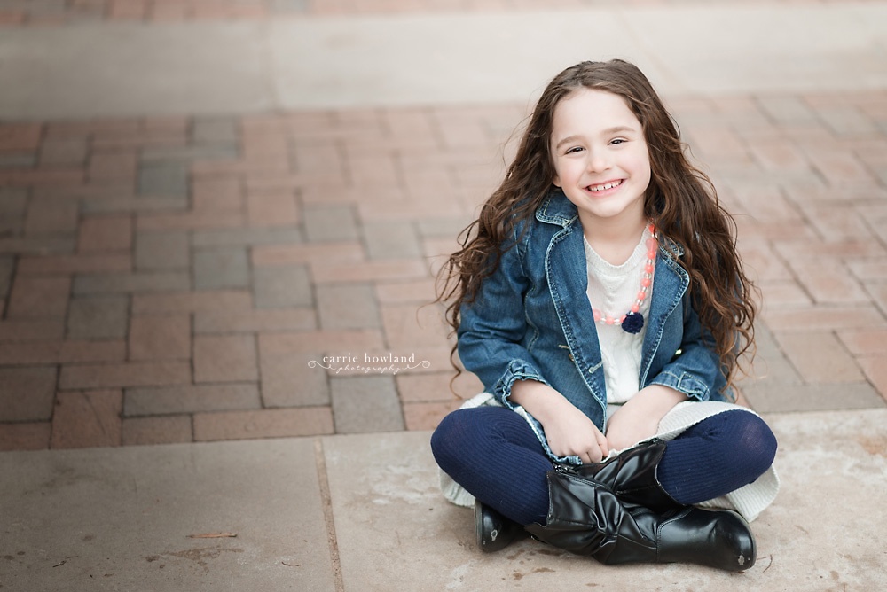 Smiling curly headed girl's headshot seated on path at Davidson college