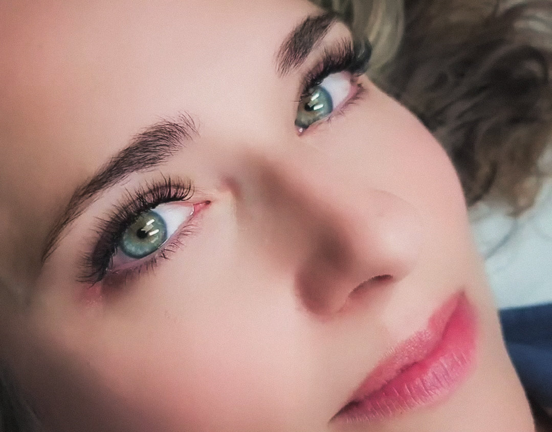 Close-up of a woman's face showing green eyes, long eyelashes, and light pink lips.