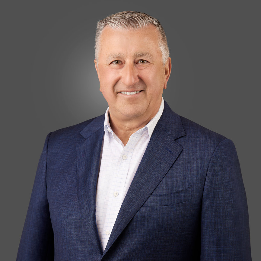Smiling man in a blue suit and white shirt against a gray background.