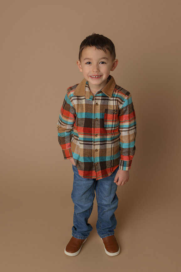 Child in a plaid shirt and jeans smiling against a beige background.