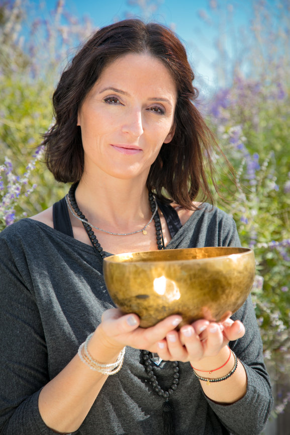 Woman holding a brass bowl outdoors, surrounded by greenery.