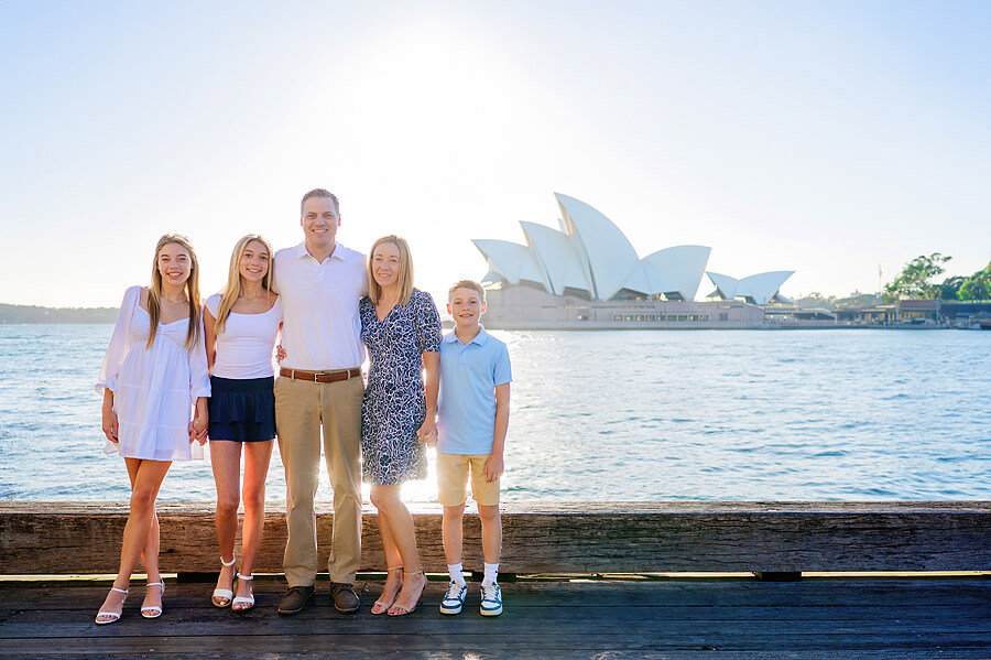 A photoshoot with a family standing beside Sydney Harbour with the Opera House behind them.