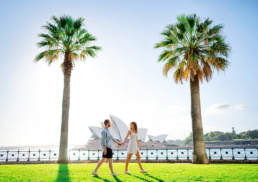 A romantic photoshoot with a couple walking in a park with the Sydney Opera House in the background.