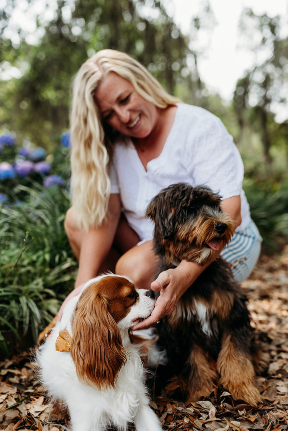 A woman in a white shirt leans over two small dogs