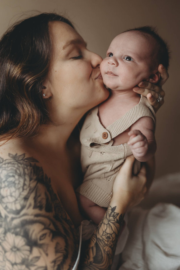 A young mother kissing her newborn on the cheek at a New Jersey baby photography session.