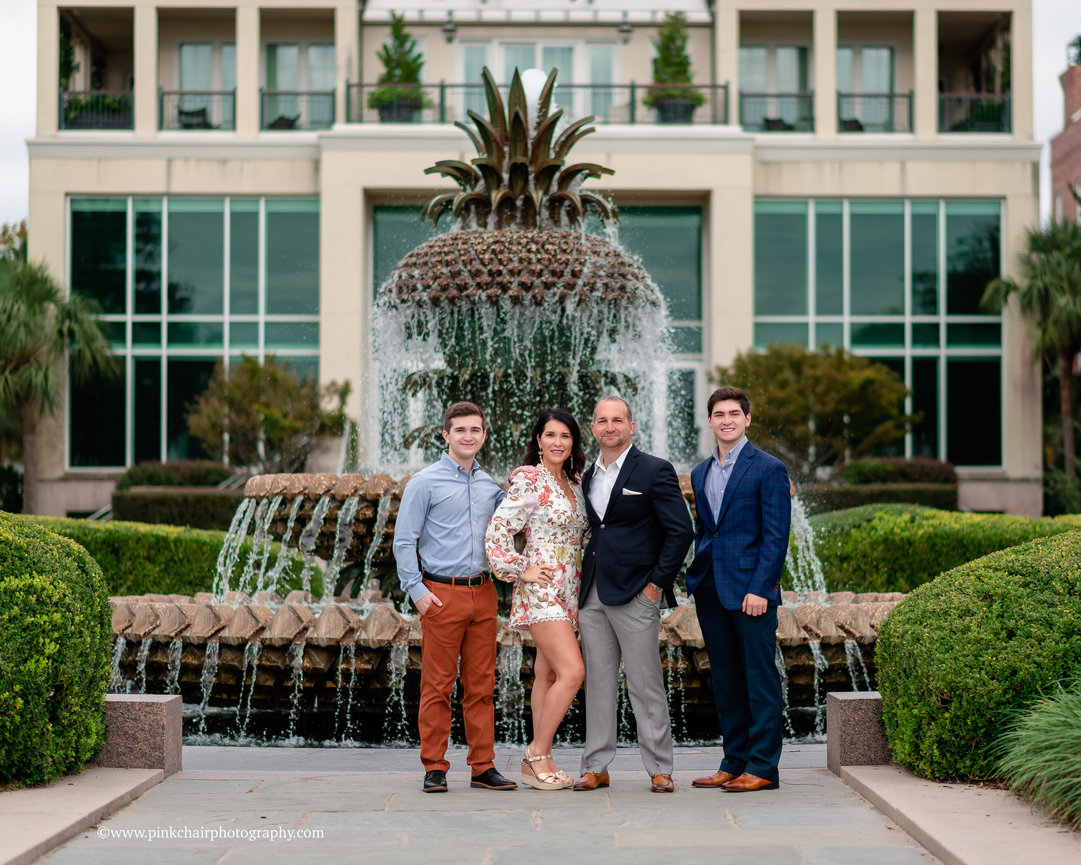 A group of four people standing in front of the pineapple fountain and a modern building.