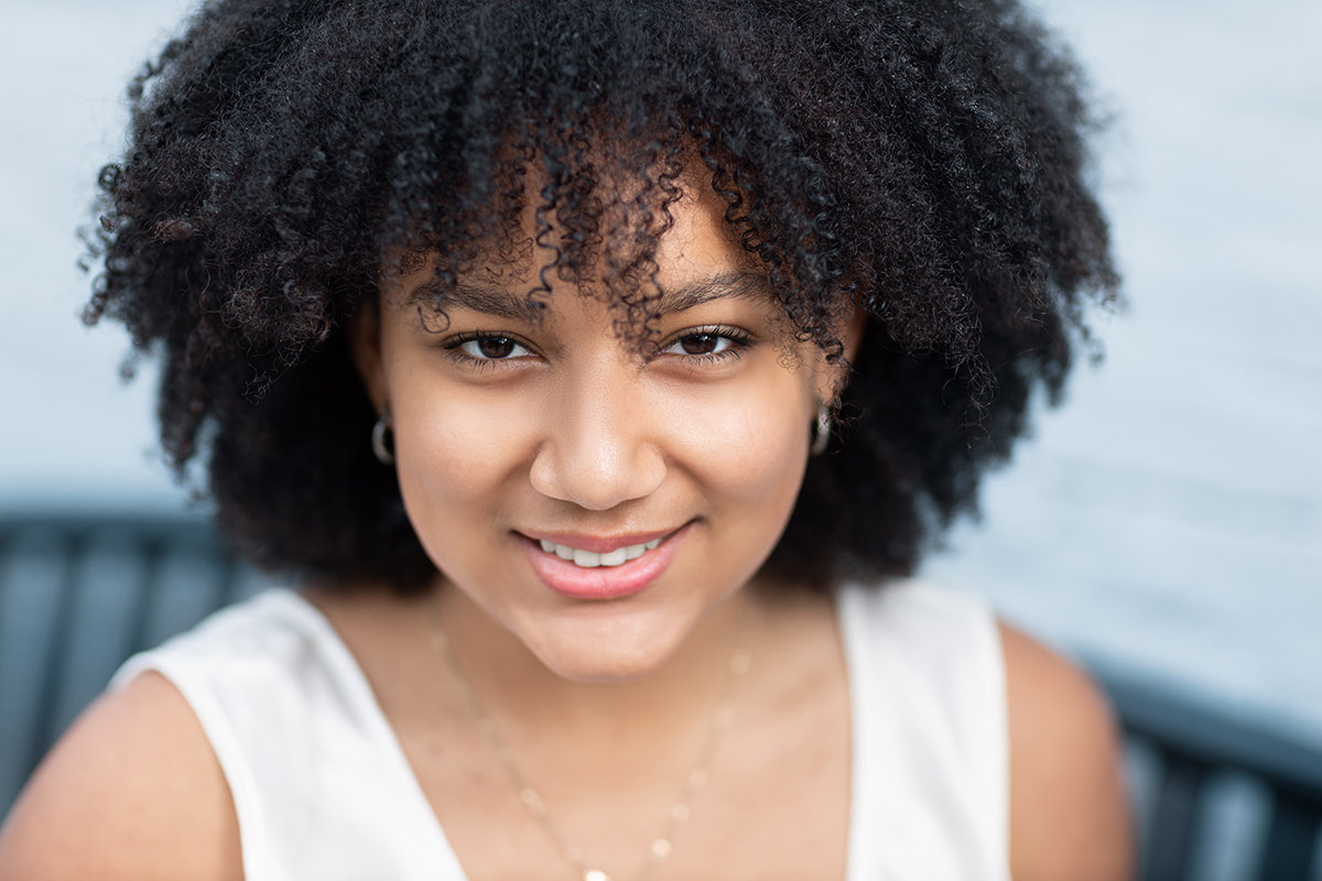 High school senior close-up portrait of a young woman smiling outdoors, captured with natural light and studio lighting, showing a warm and genuine expression
