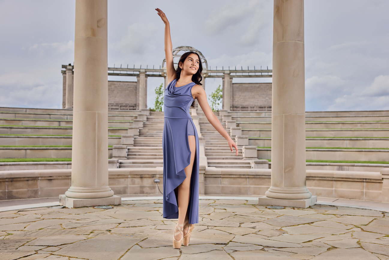 Ballerina senior portrait at Coxhall Gardens in Carmel, Indiana, standing en pointe in a flowing blue dress beneath the columns of the Centerpiece.