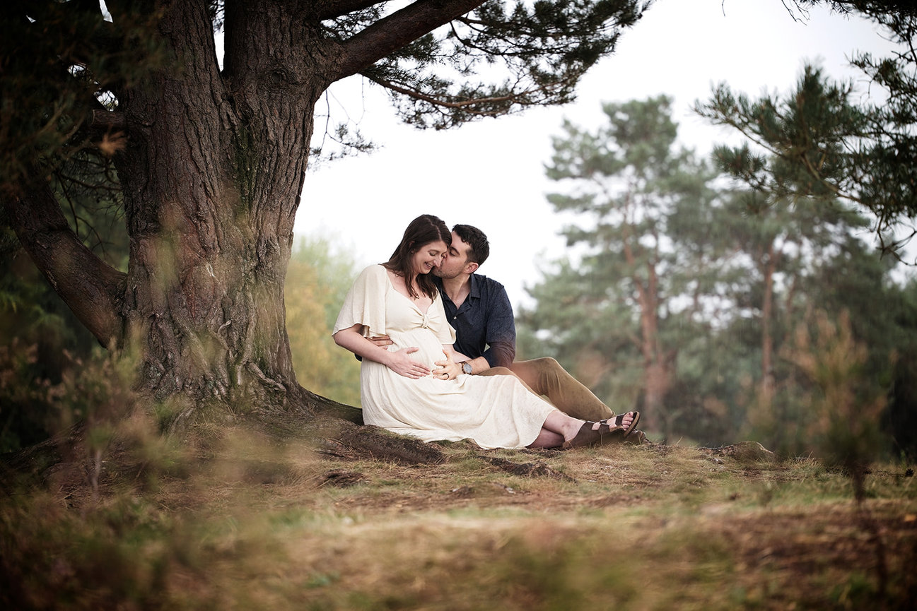 Expectant couple sitting together under a large tree outdoors