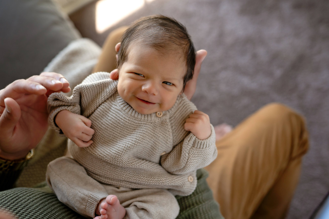 Smiling baby in a knit outfit being held on an adult's lap indoors