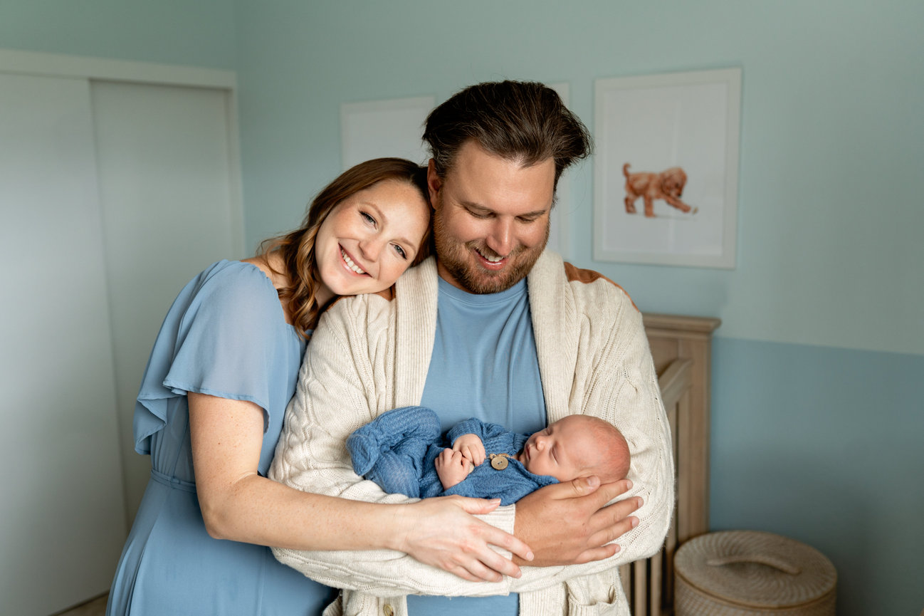 Smiling parents hold their sleeping newborn in a cozy nursery.
