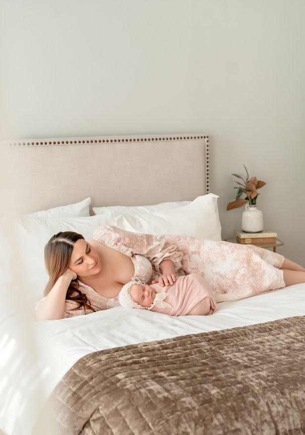 Mother lying with sleeping newborn on a bed in a bright, softly styled bedroom