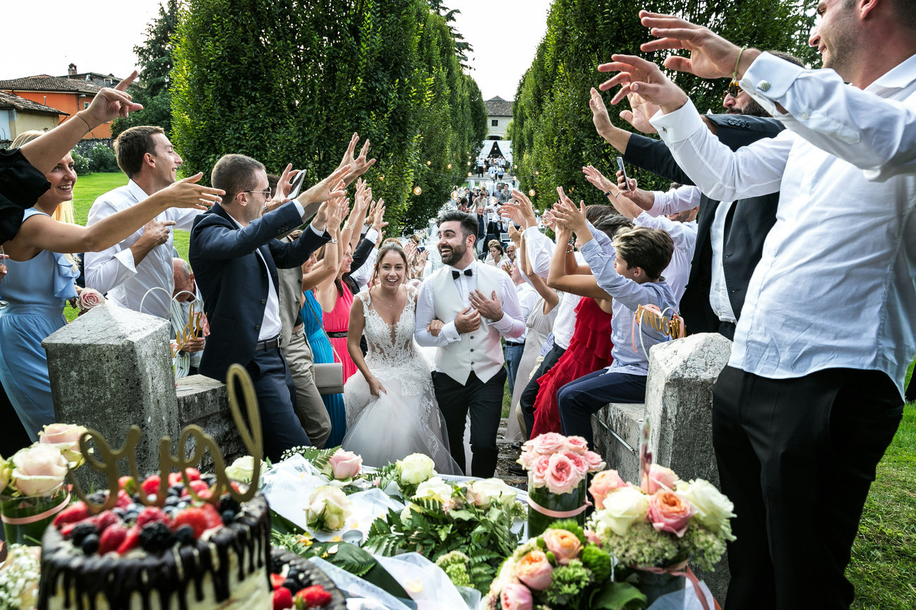 Wedding guests cheer during a lively outdoor toast at the reception table.