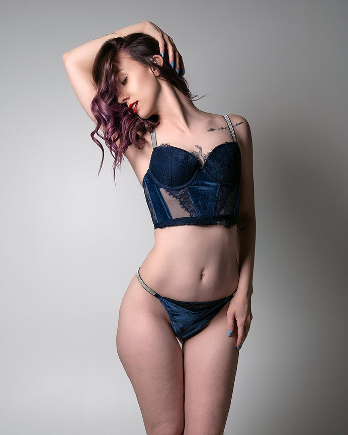 Elegant portrait of a model in navy blue lingerie, striking a confident pose with soft lighting against a neutral background. Captured by Tre Nelson Photography in Sandy, Utah, showcasing beauty, style, and poise.