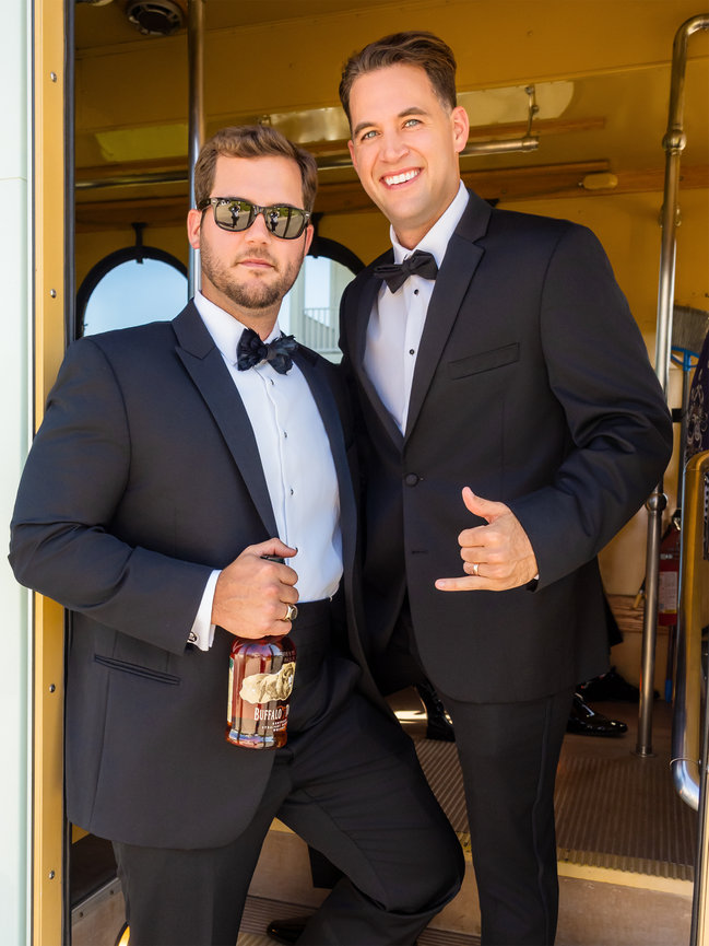 Groom poses with best man wearing tuxedos and holding a bottle of Buffalo Trace.