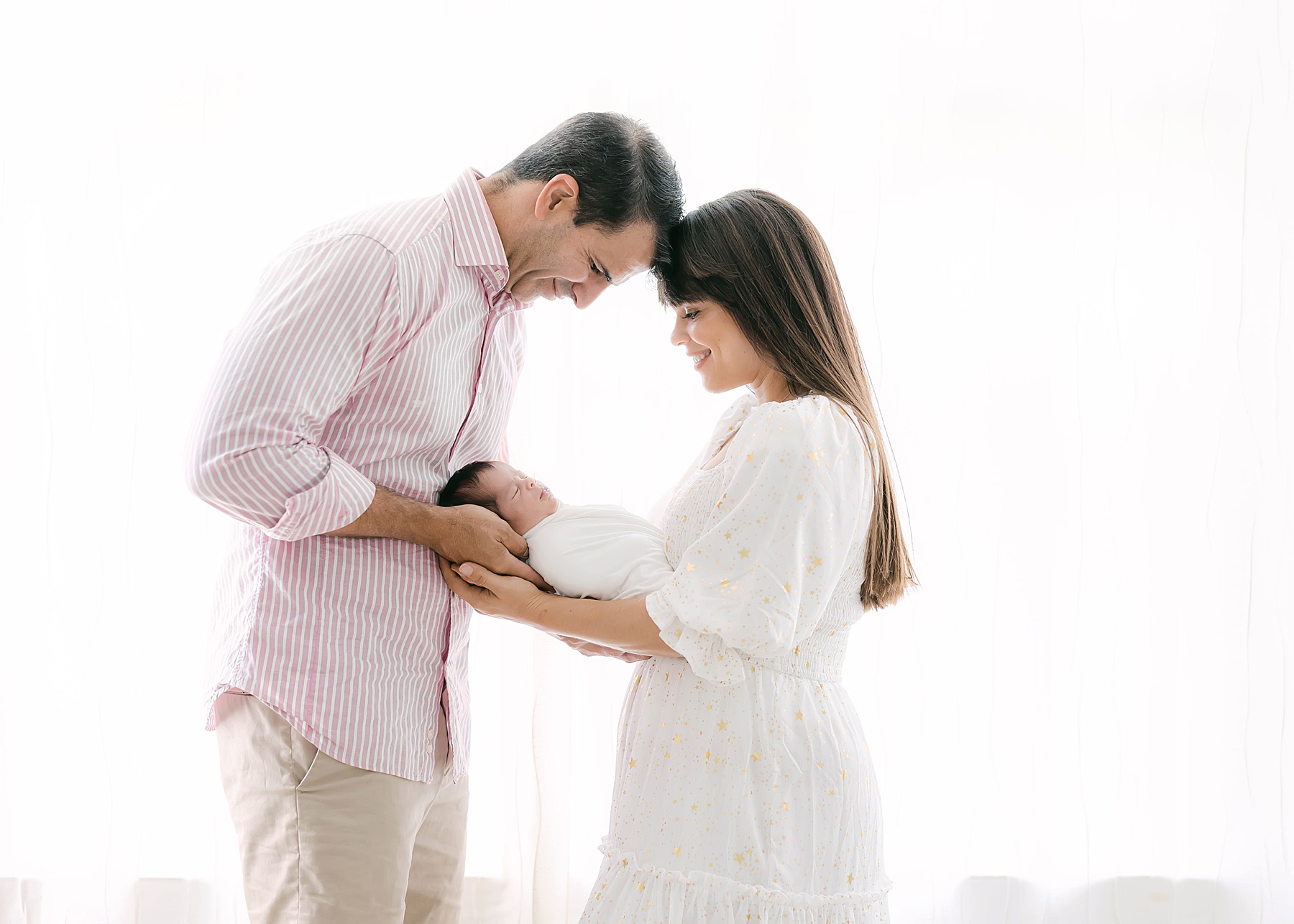 couple holding newborn baby in front of window light