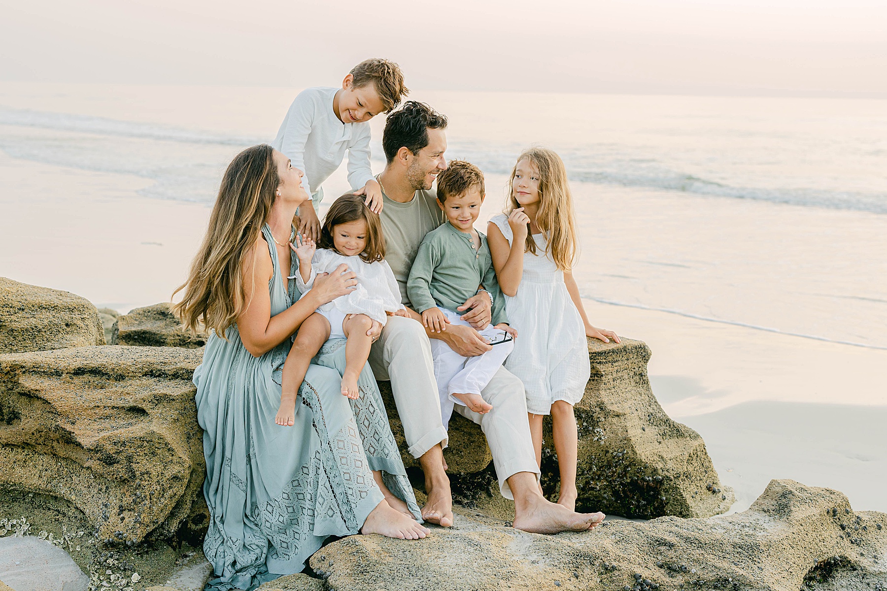 family of six sitting on the rocks at the beach