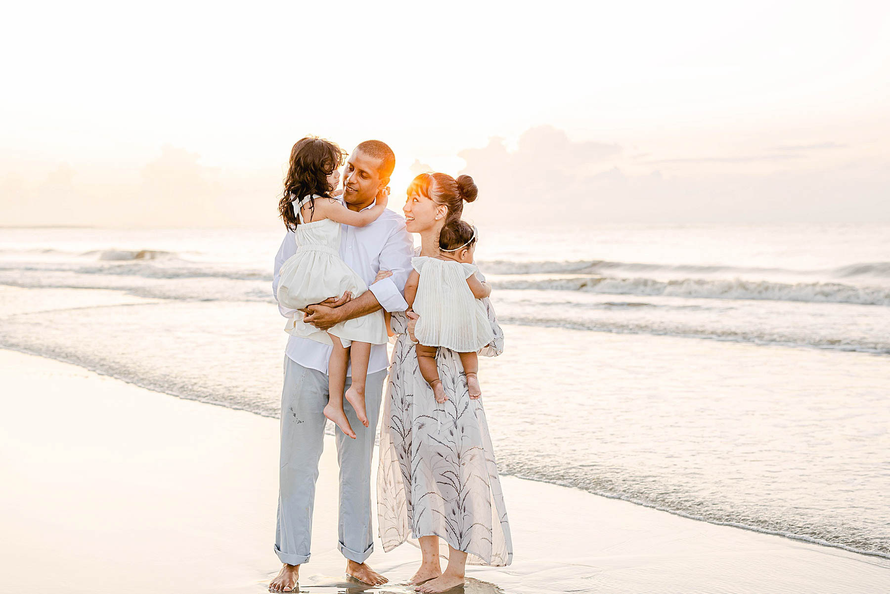 family standing barefoot on the beach at sunrise