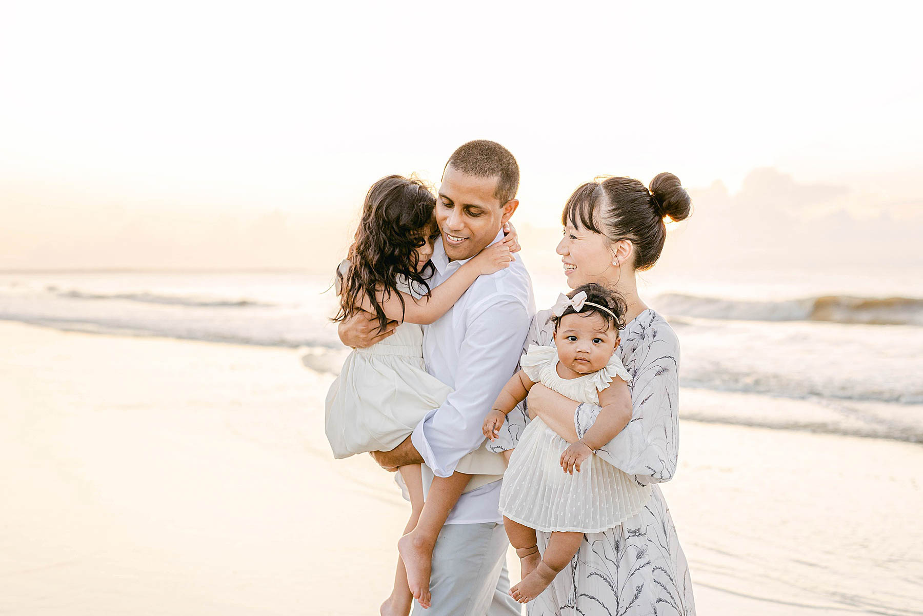 family holding babies on the beach at sunrise wearing neutral colors