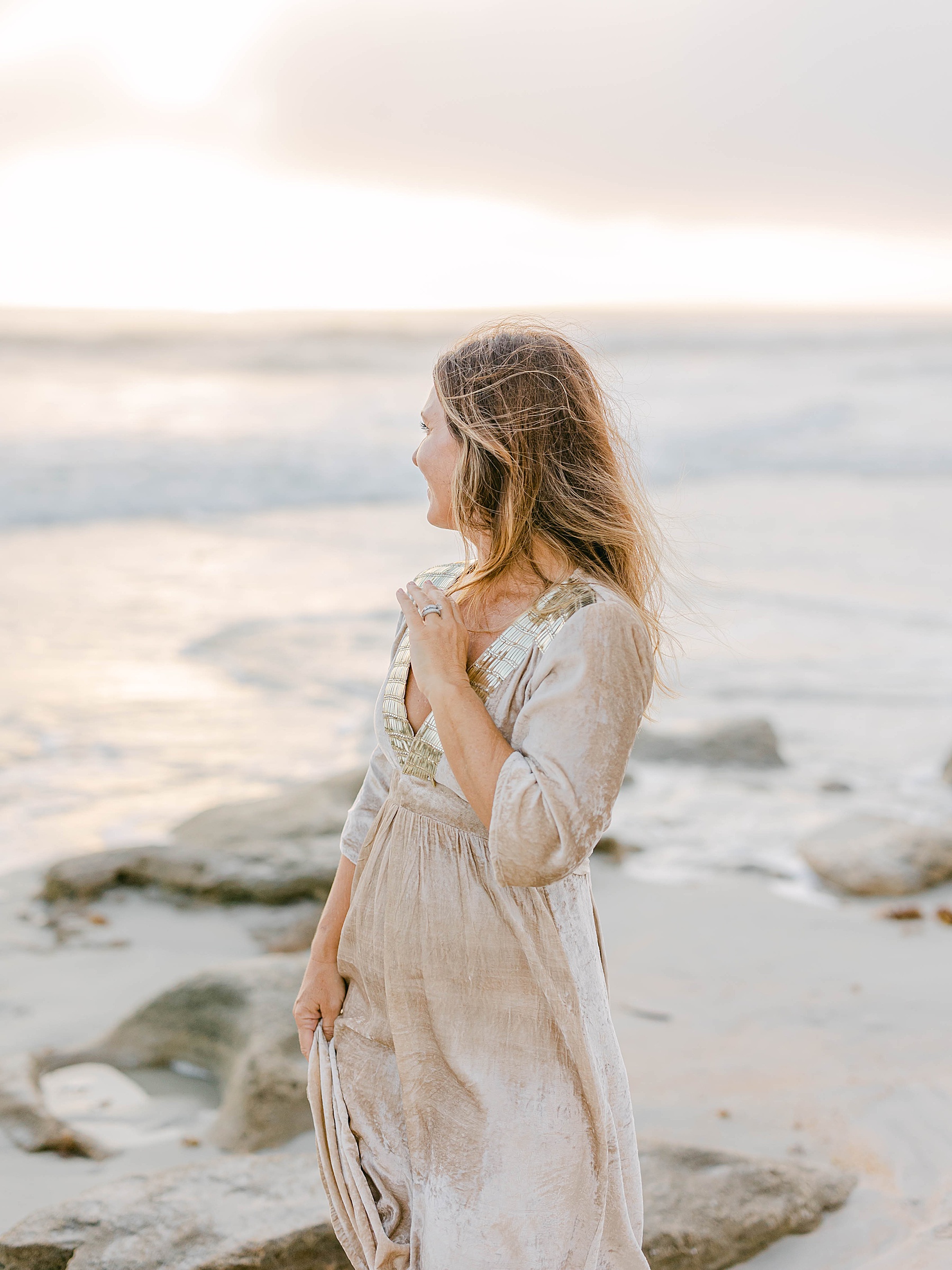 woman standing on a rock at the beach at sunrise in a maxi shimmer dress