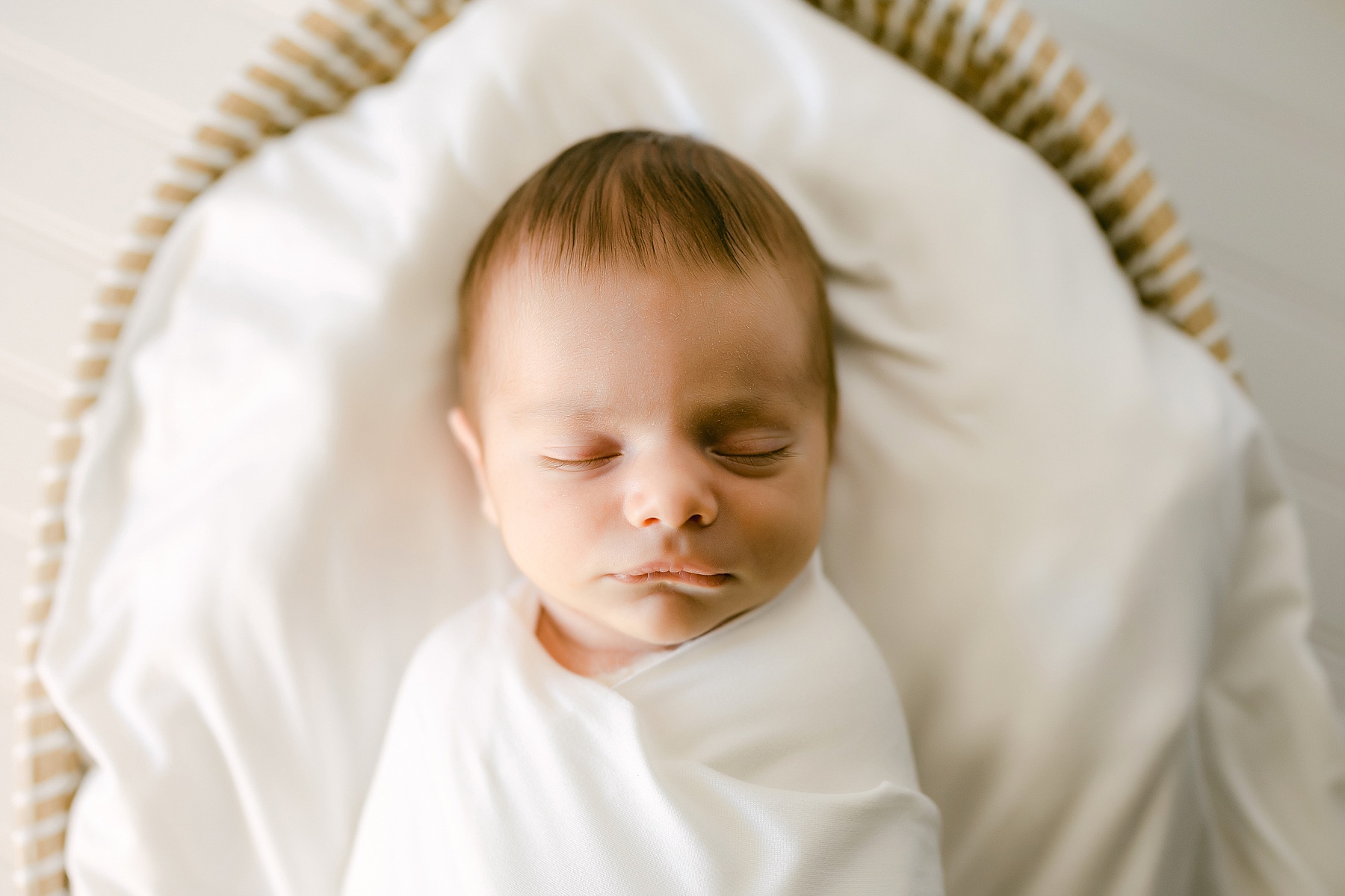 newborn baby boy sleeping in wicker basket wrapped in a white blanket