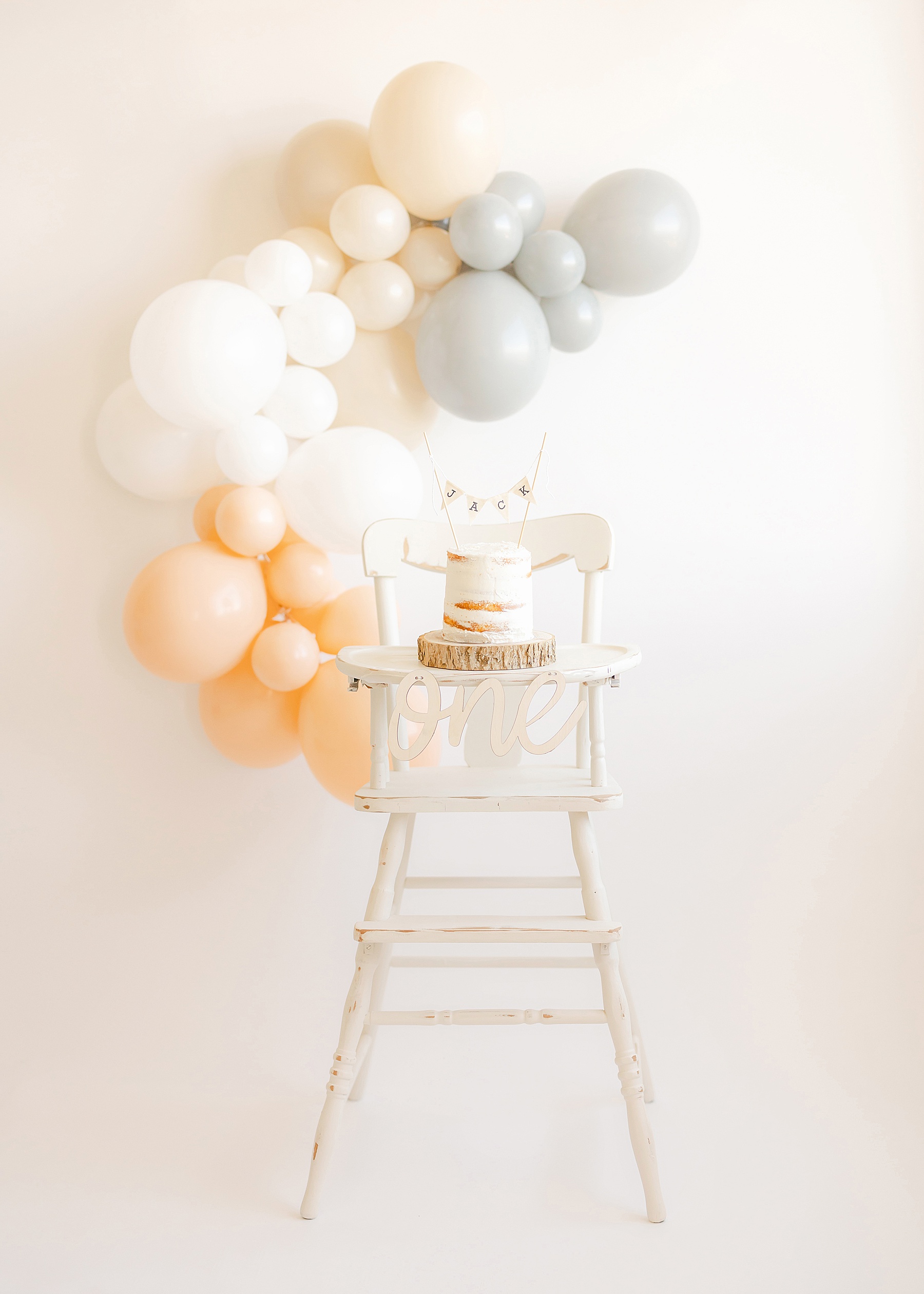 white high chair with balloons in background with small white cake in front