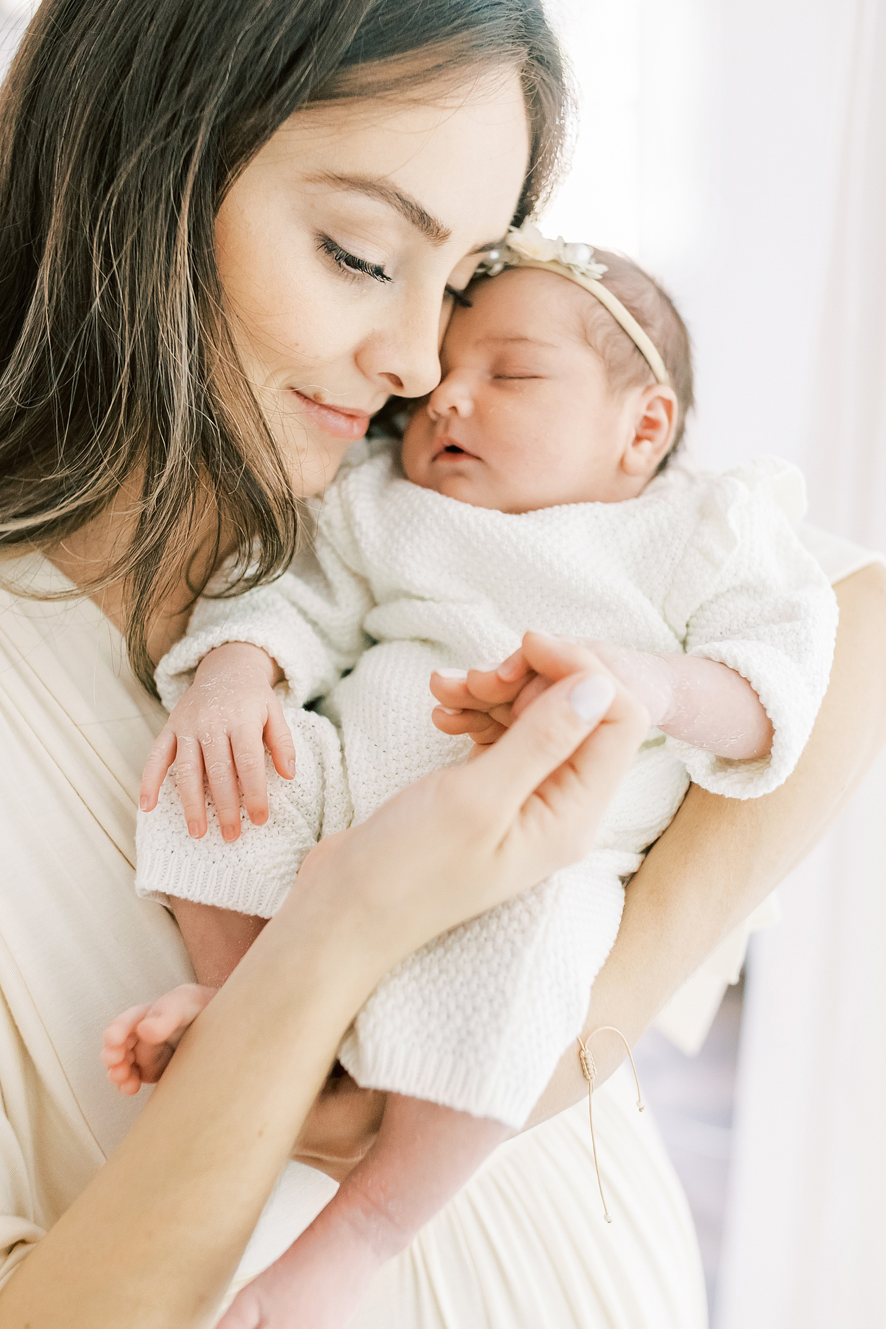 woman in cream dress holding newborn baby girl hand