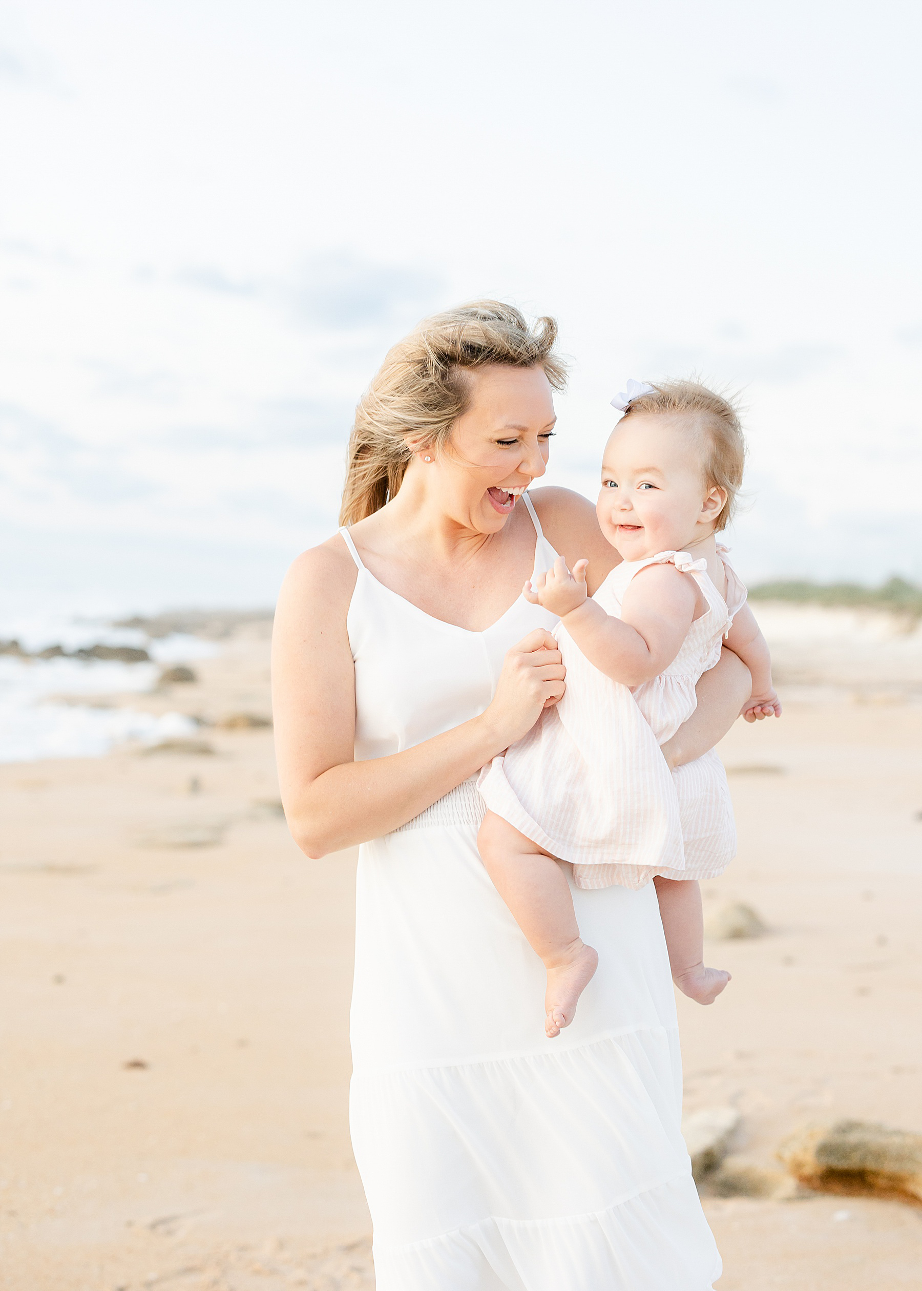 woman holding baby girl on the beach at sunrise wearing long white dress