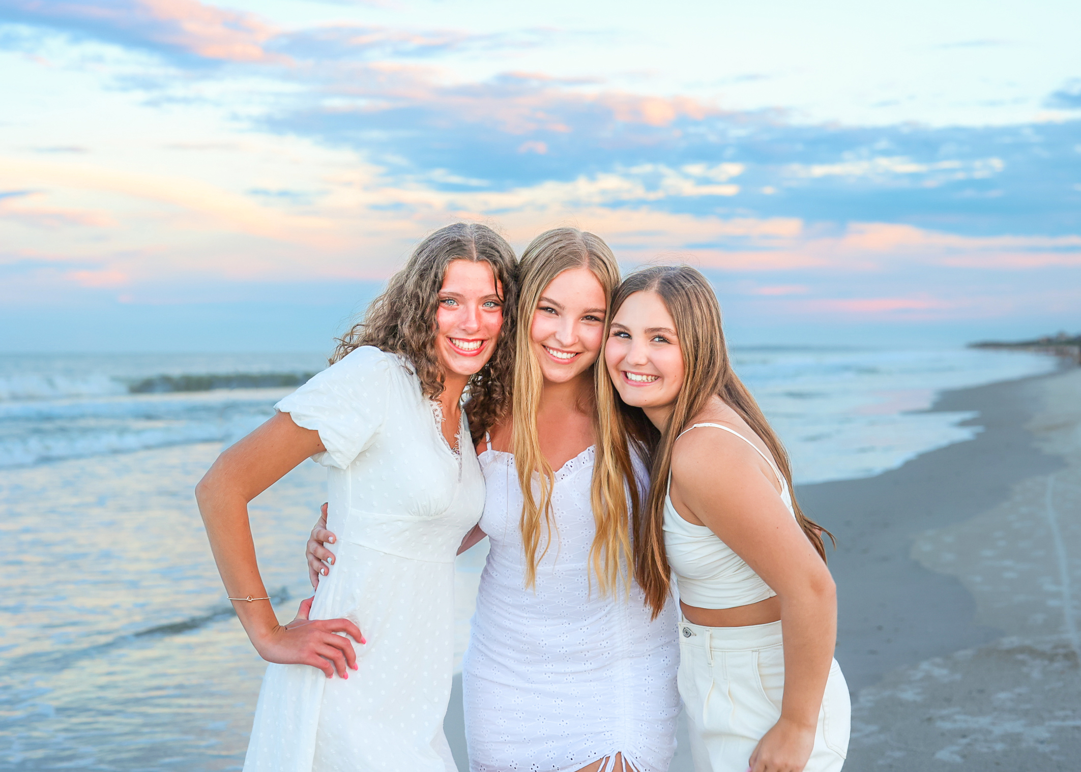 three young woman dressed in white for family portraits at sunset on the beach in Amelia Island Florida
