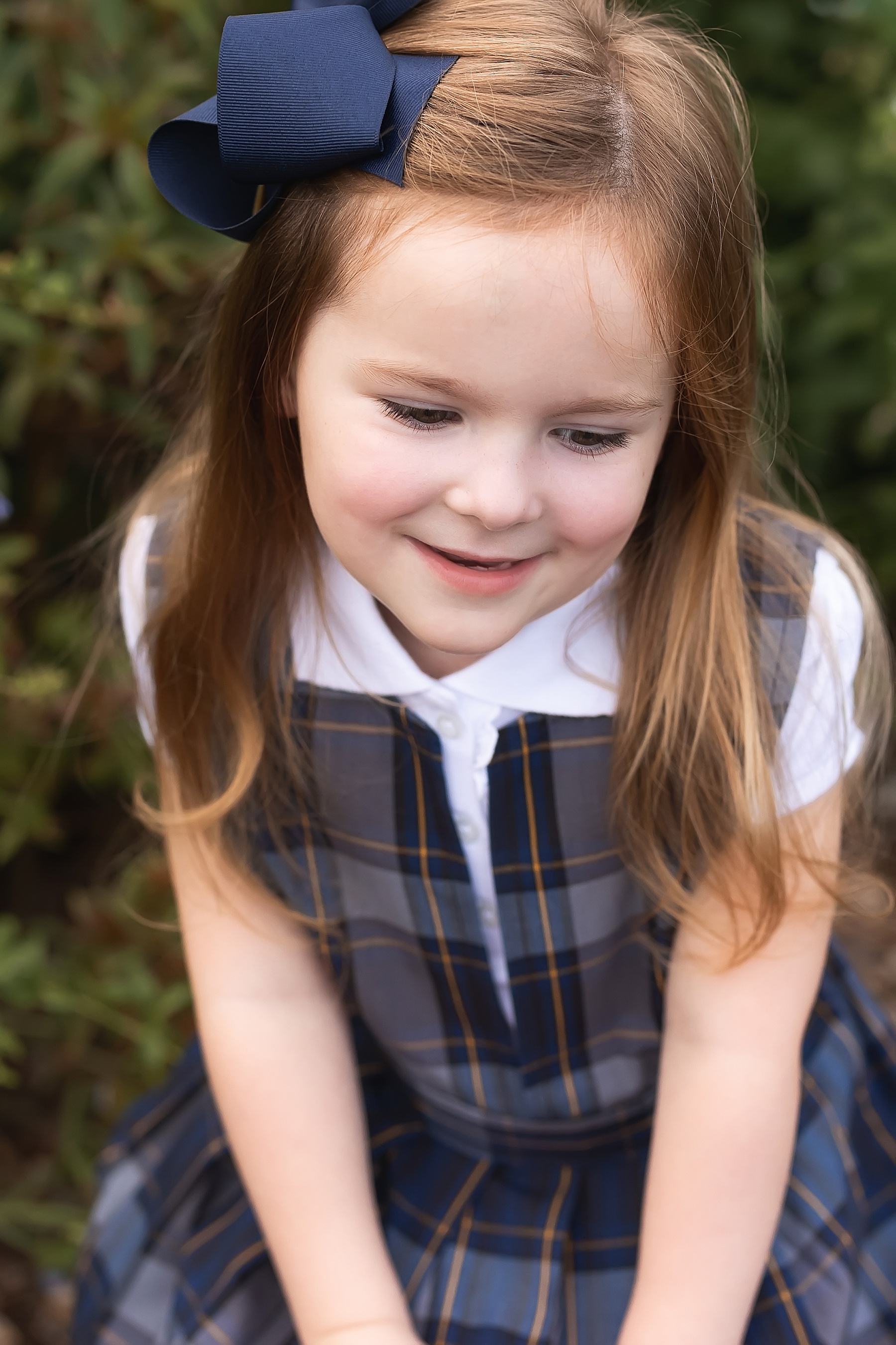 little girl dressed in navy and white plaid with red hair holding pre-school sign
