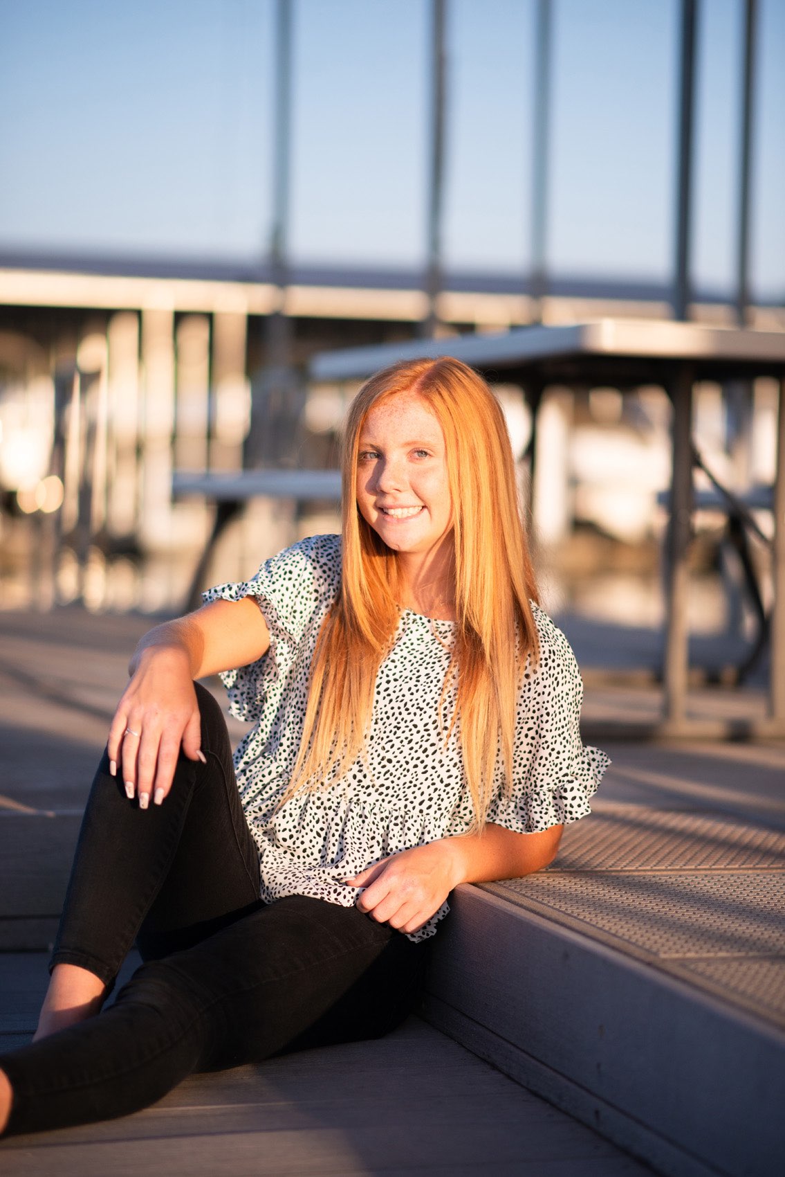 Senior girl in printed top sitting on a dock at Tablerock Lake.