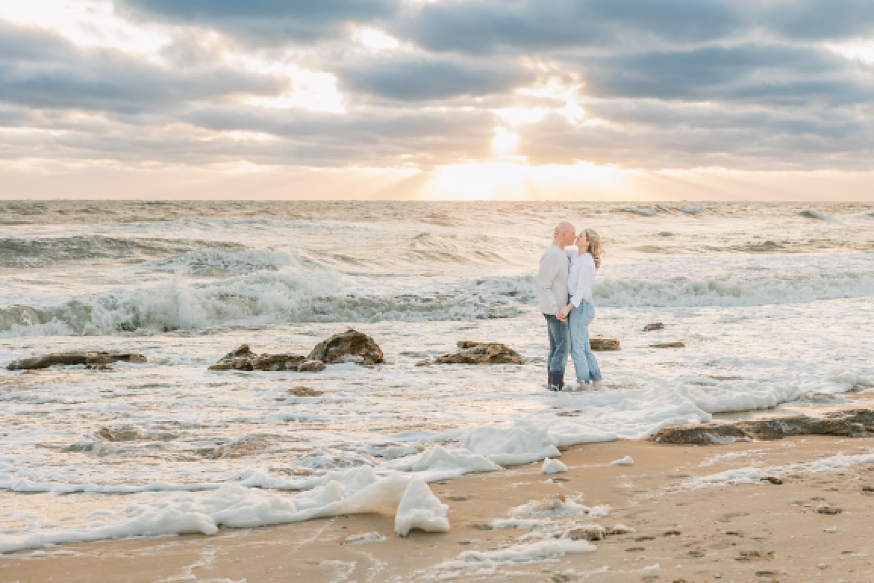 couples in jeans and white shirts holding each other in the water at sunrise on the beach