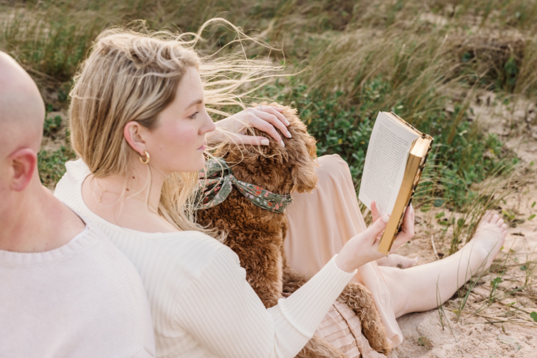 woman reading book on the beach at sunrise petting golden doodle dog