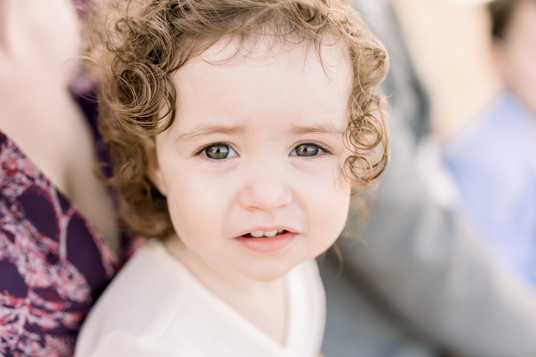 little girl looking directly at the camera in cream dress with curly brown hair