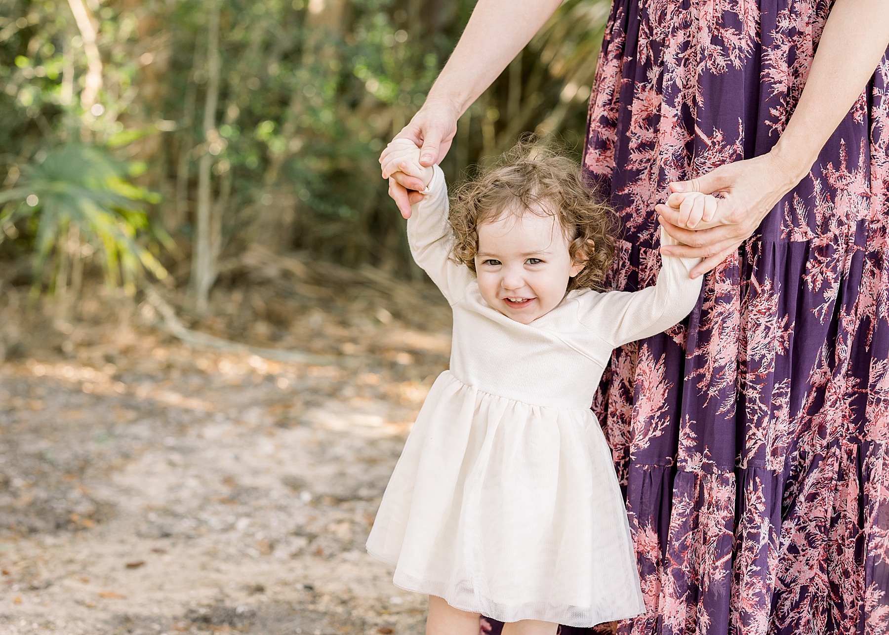 little girl in cream dress smiling walking with mom holding her hands