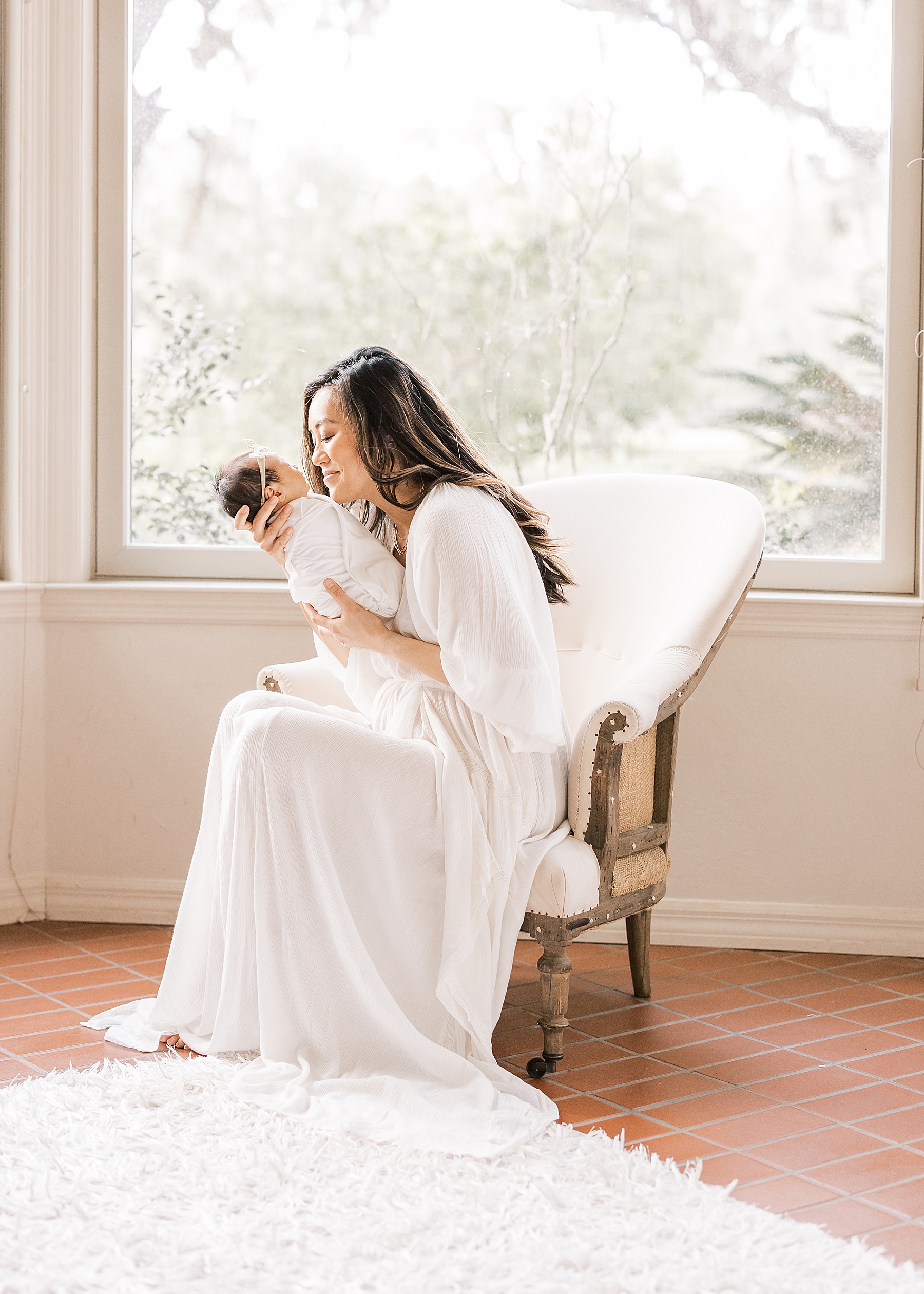 woman in white maxi dress sitting on deconstructed chair kissing newborn baby girl
