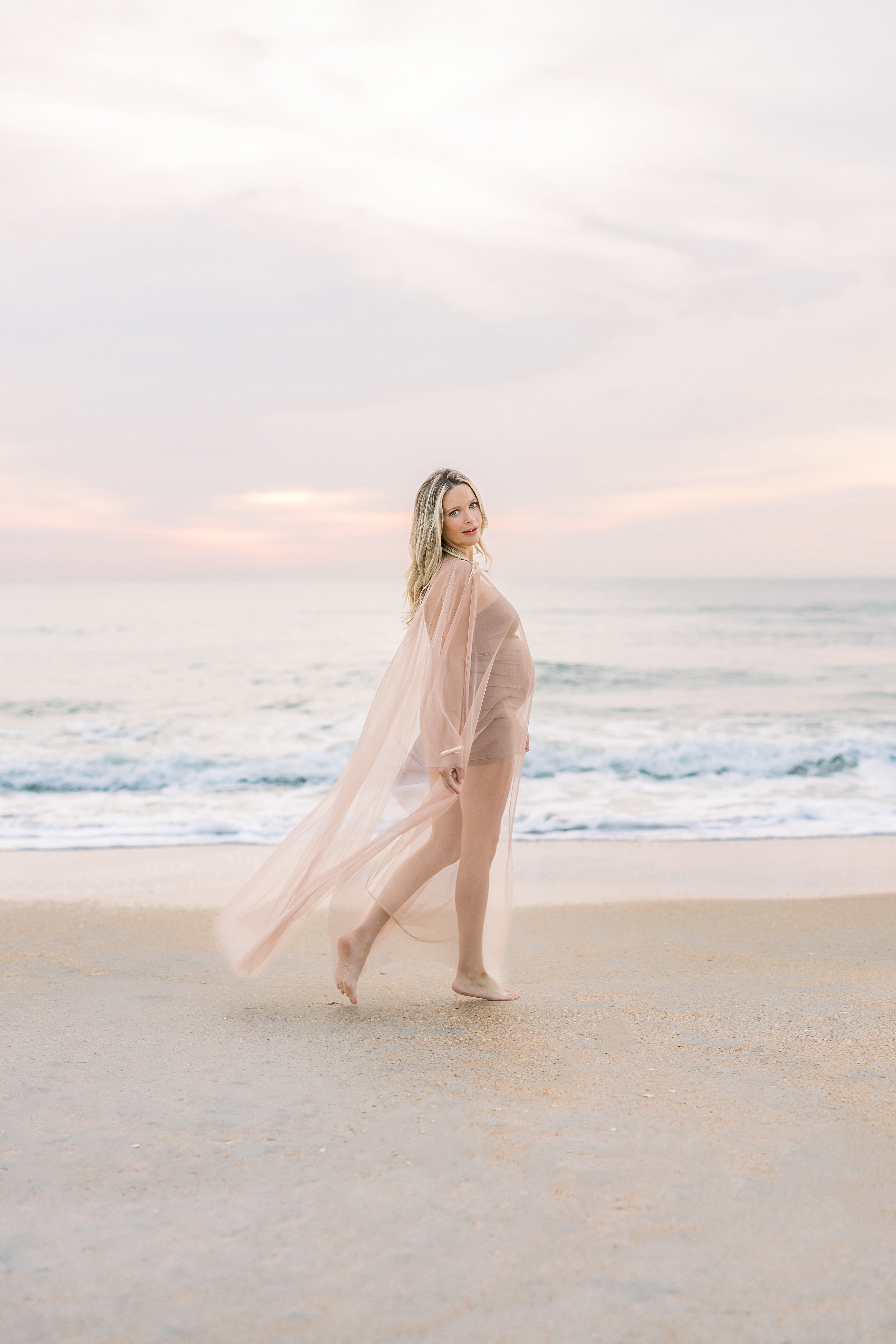 blonde pregnant woman standing on the beach at sunrise
