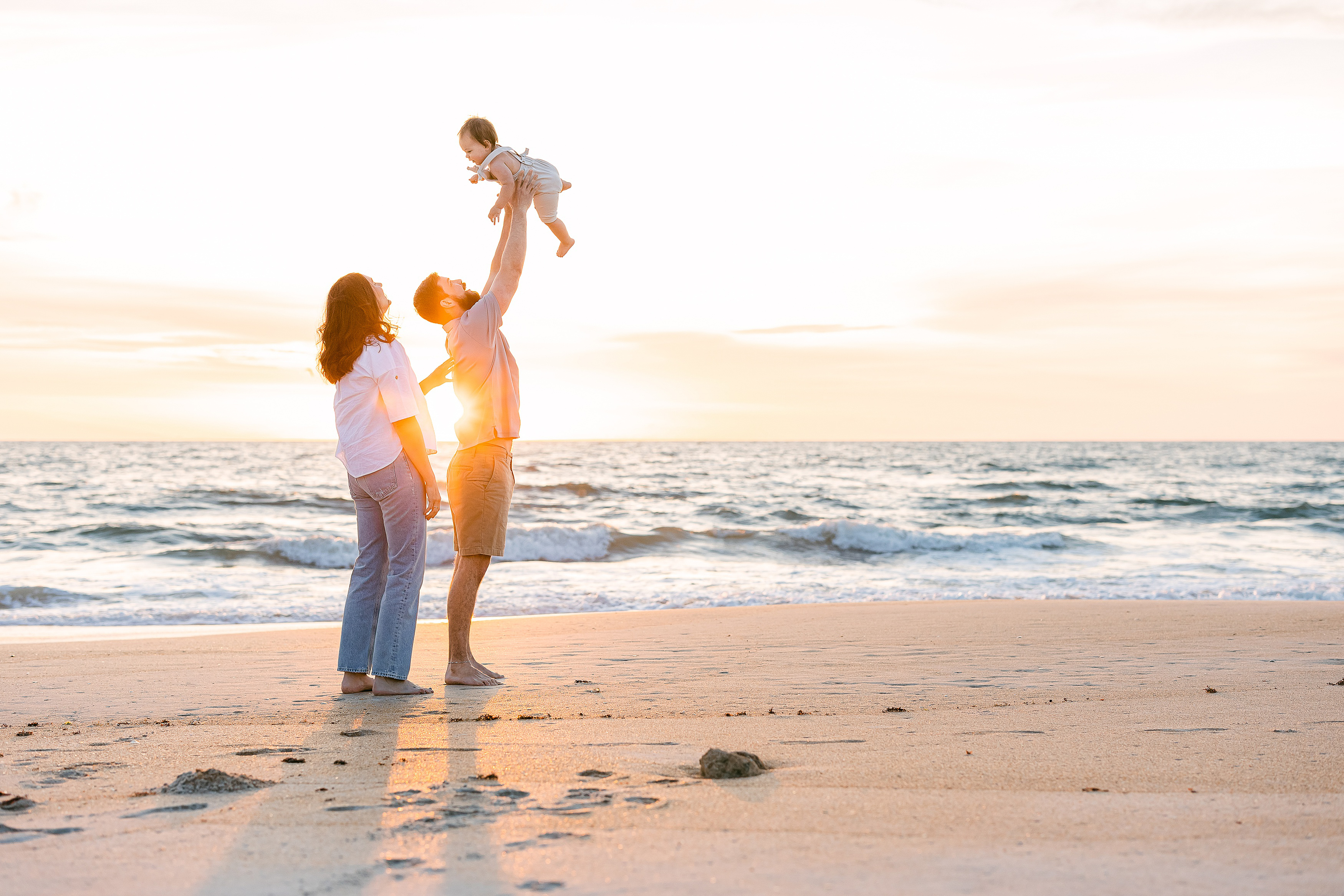 family holding baby boy in the air on the beach at sunrise in St. Augustine Beach