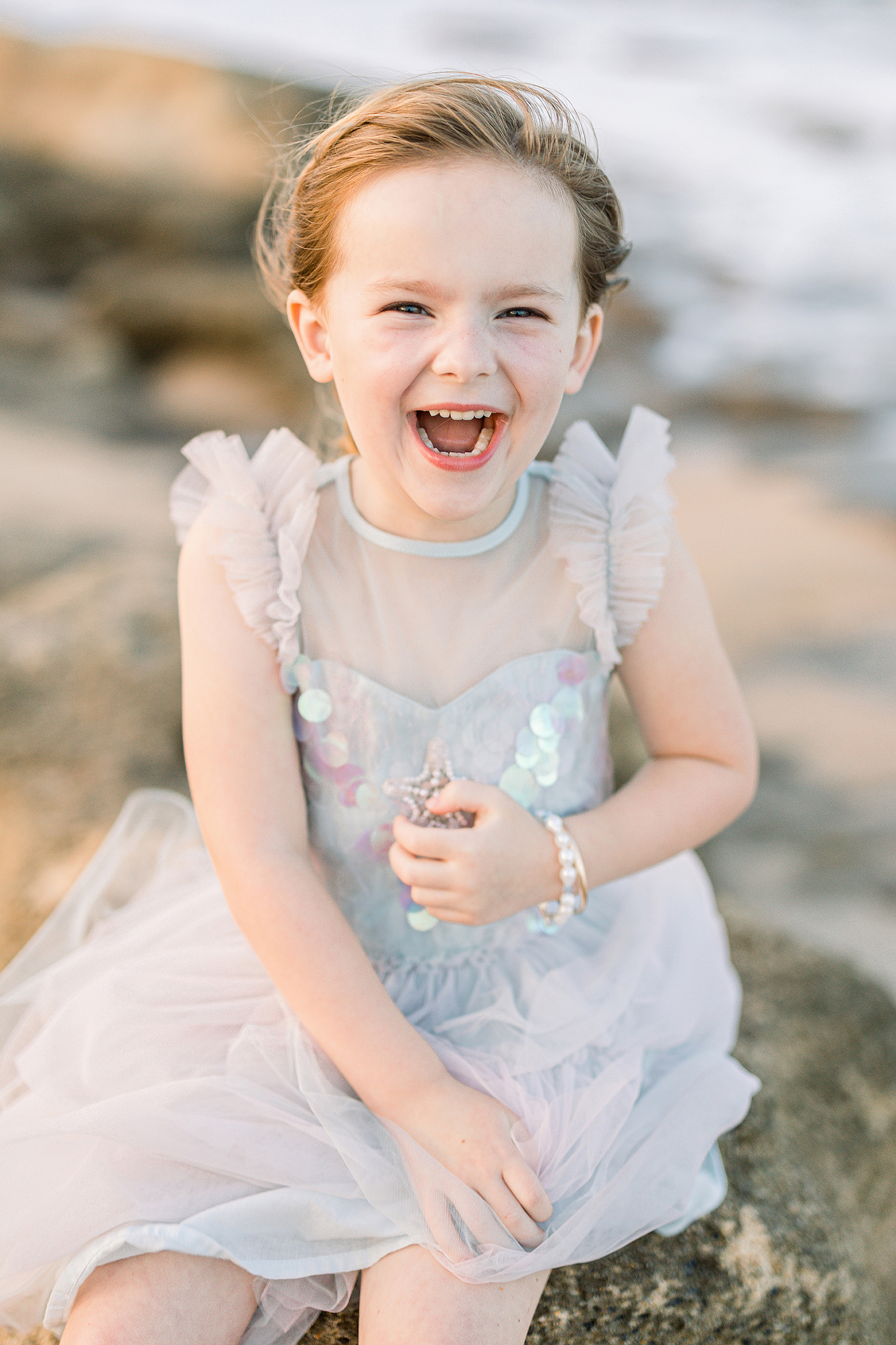 little girl laughing at the beach on the rocks during sunset