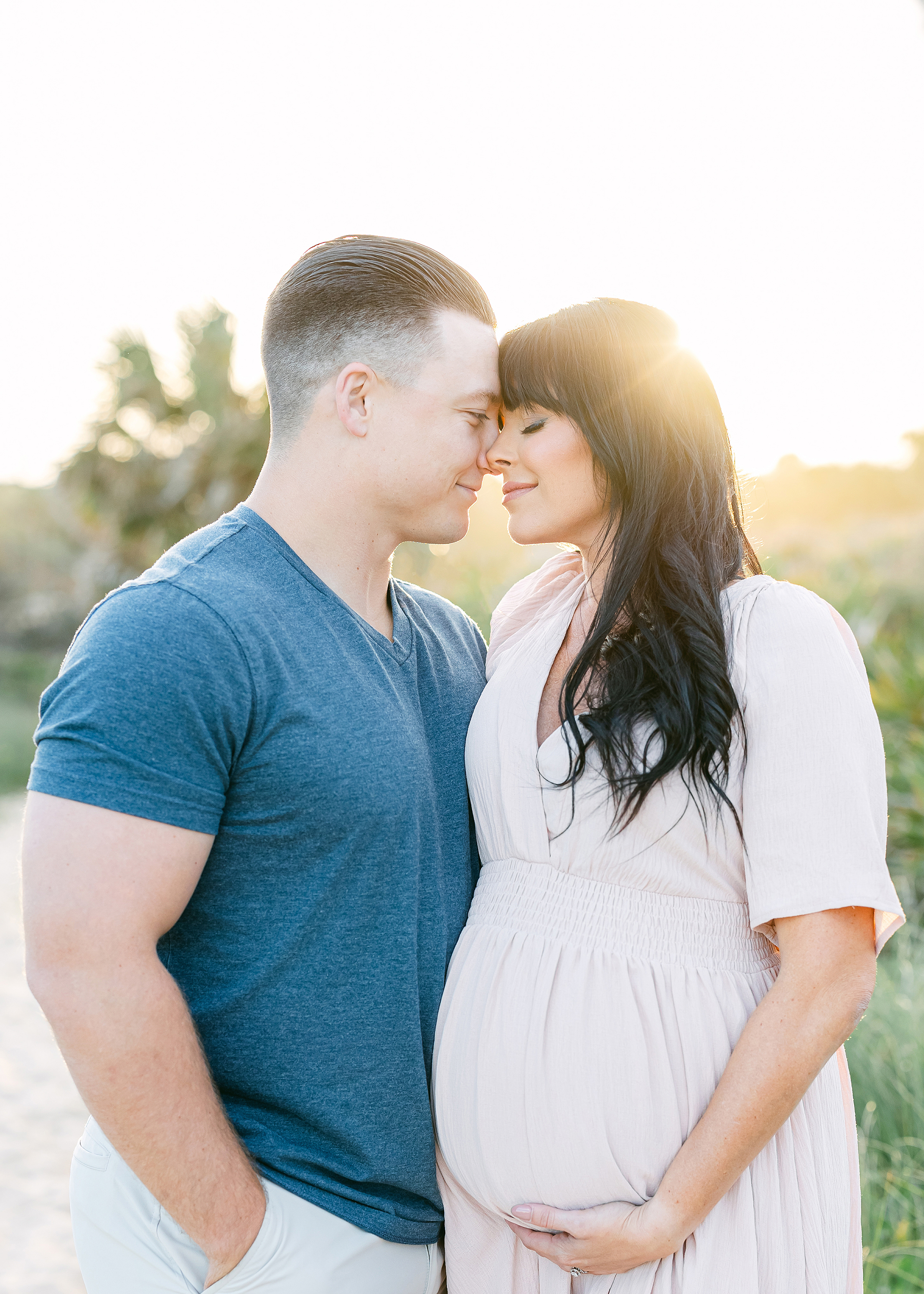 Airy maternity portrait of a man and woman on the beach at sunset.