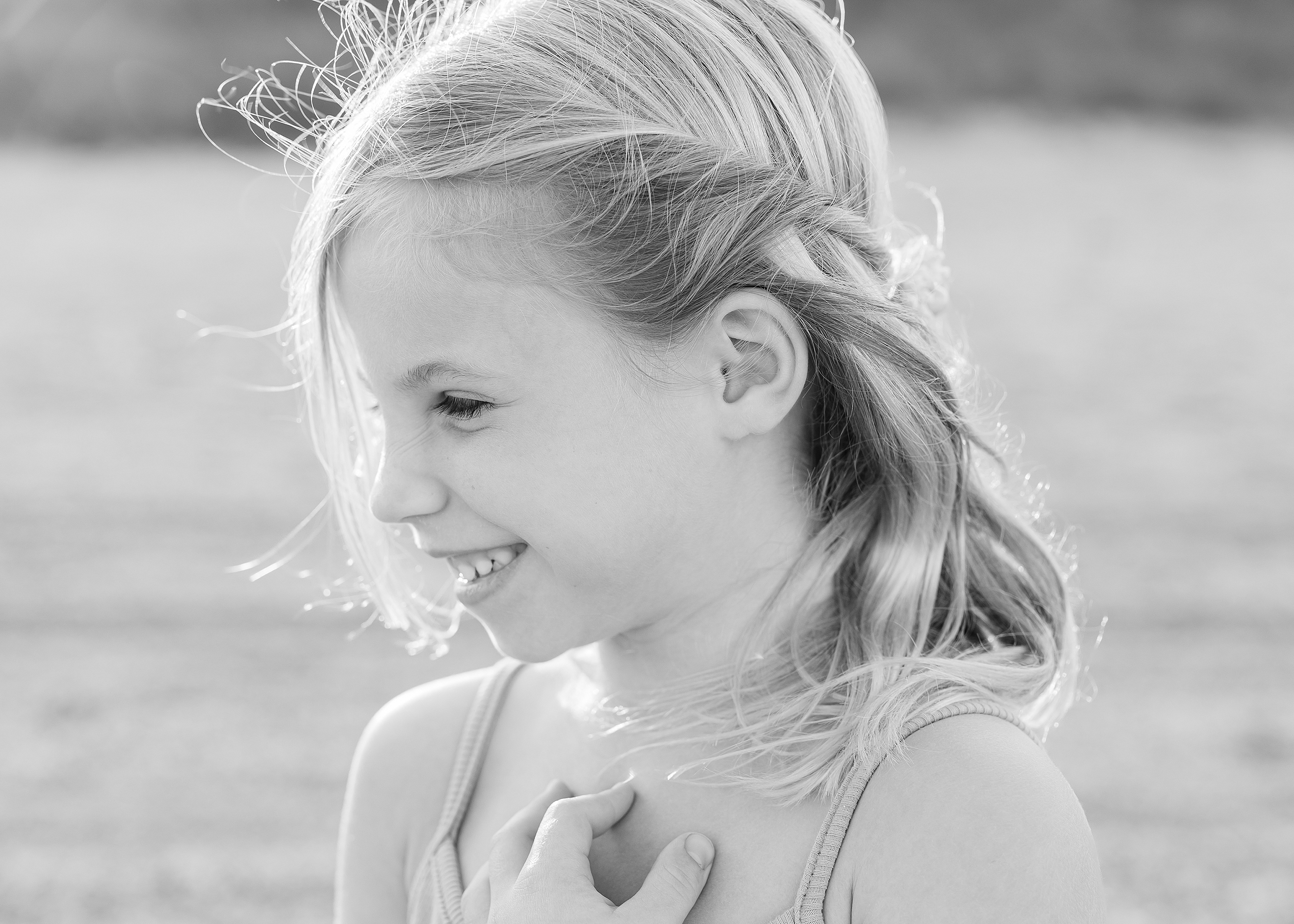 Black and white beach portrait of a little girl with blonde hair smiling.