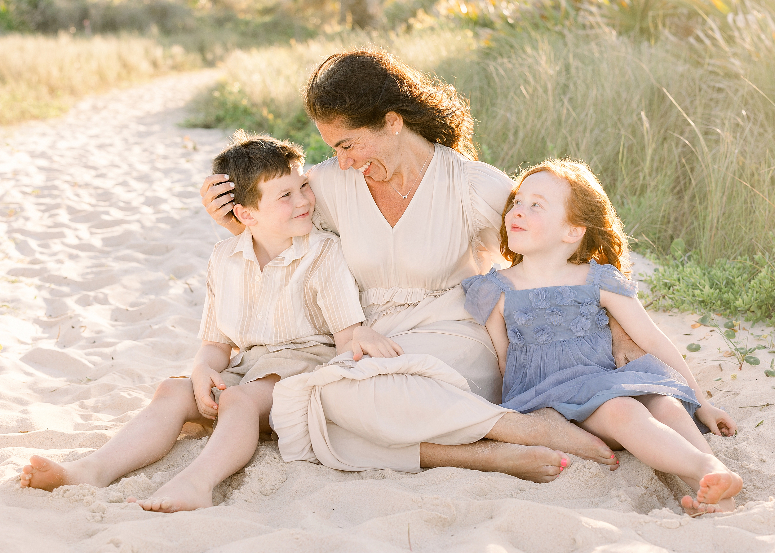 A mother sits on the sand at St. Augustine Beach with her two children at sunset. 