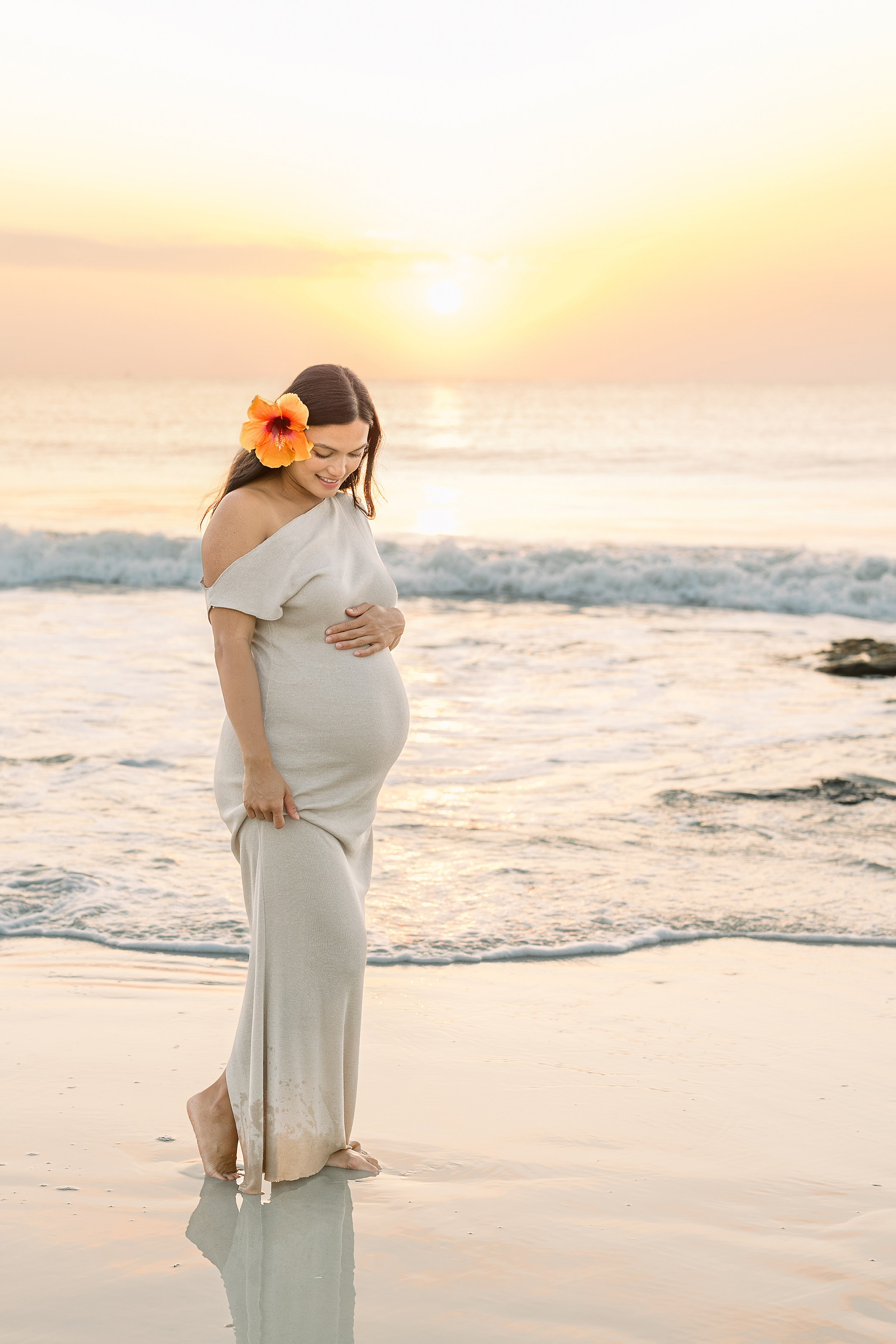 A colorful sunrise maternity portrait of a woman with a flower in her hair on Saint Augustine Beach.