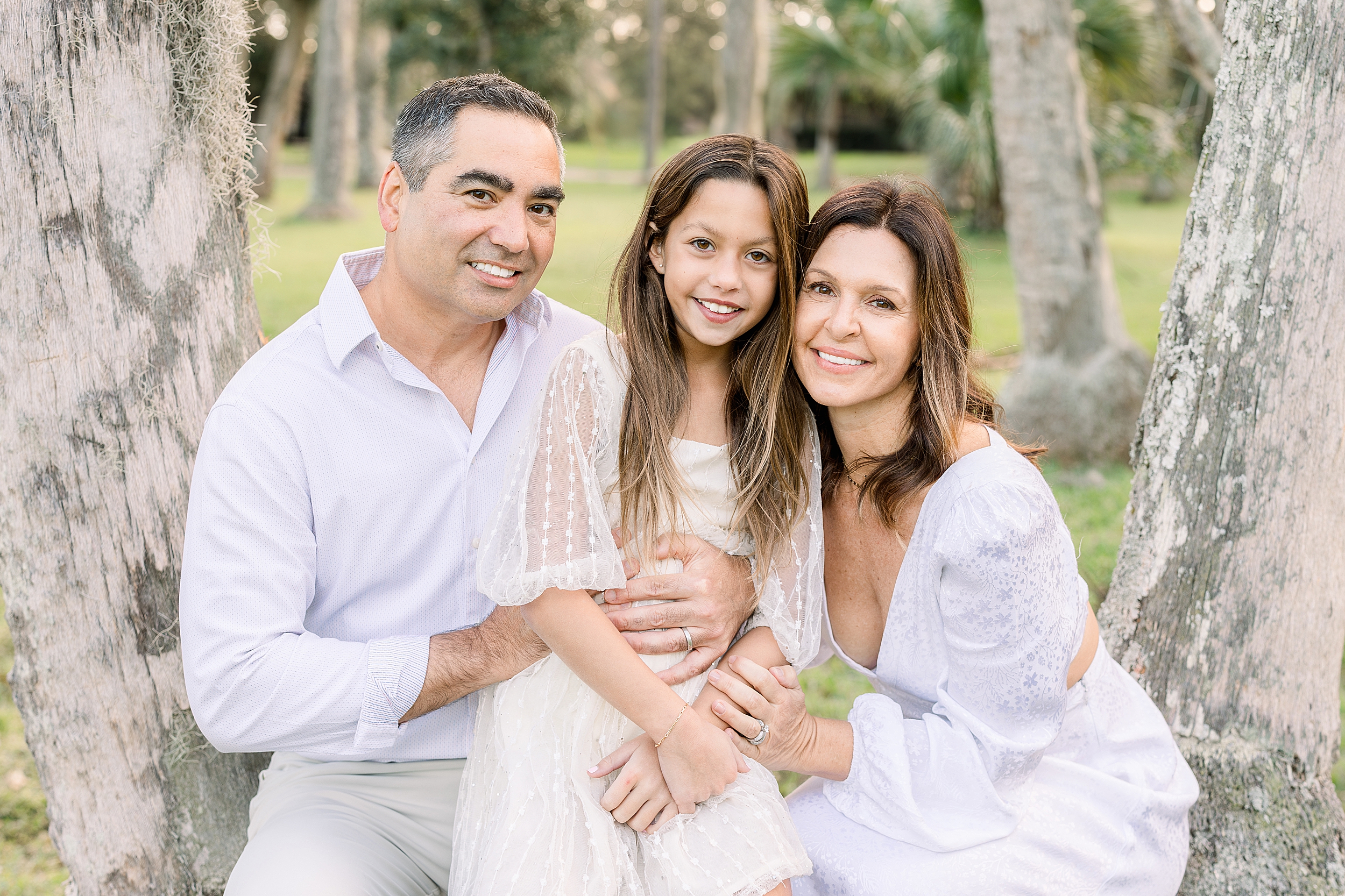 A light and airy family portrait of a family of three sitting amongst the tress in Johansen Park.