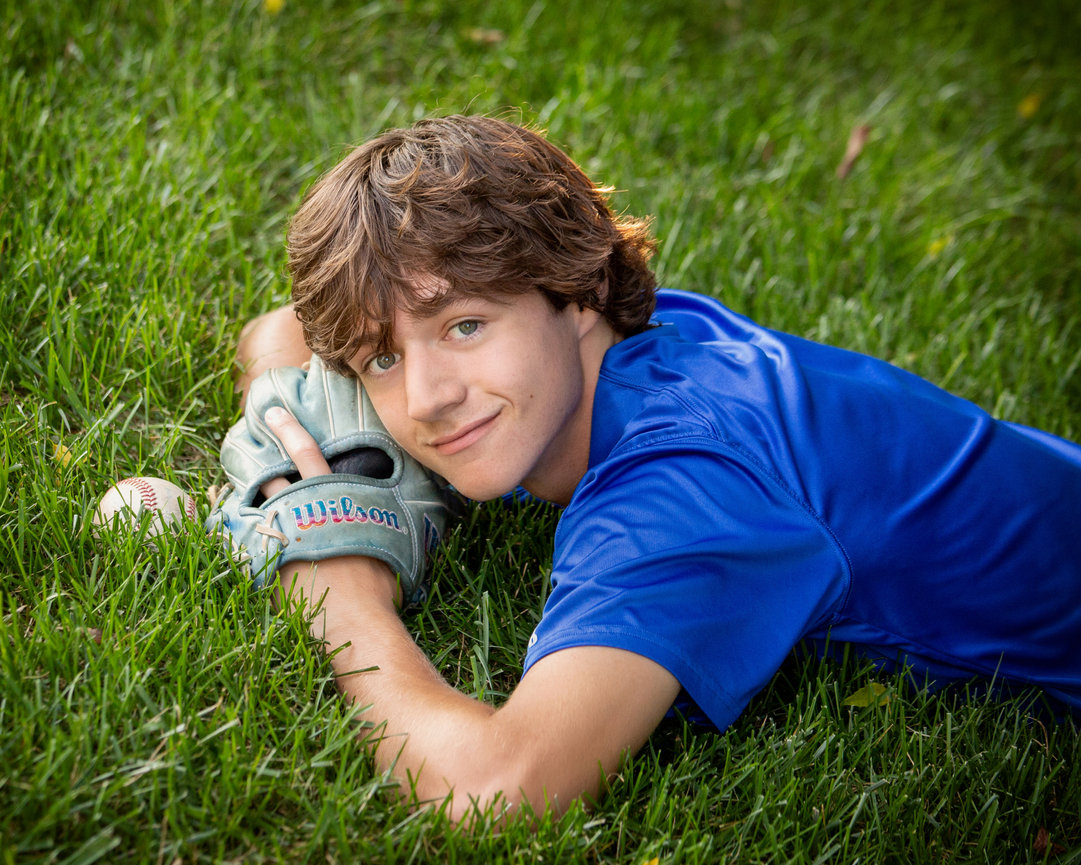 Teen boy in blue shirt lying on grass with a baseball glove and ball nearby.