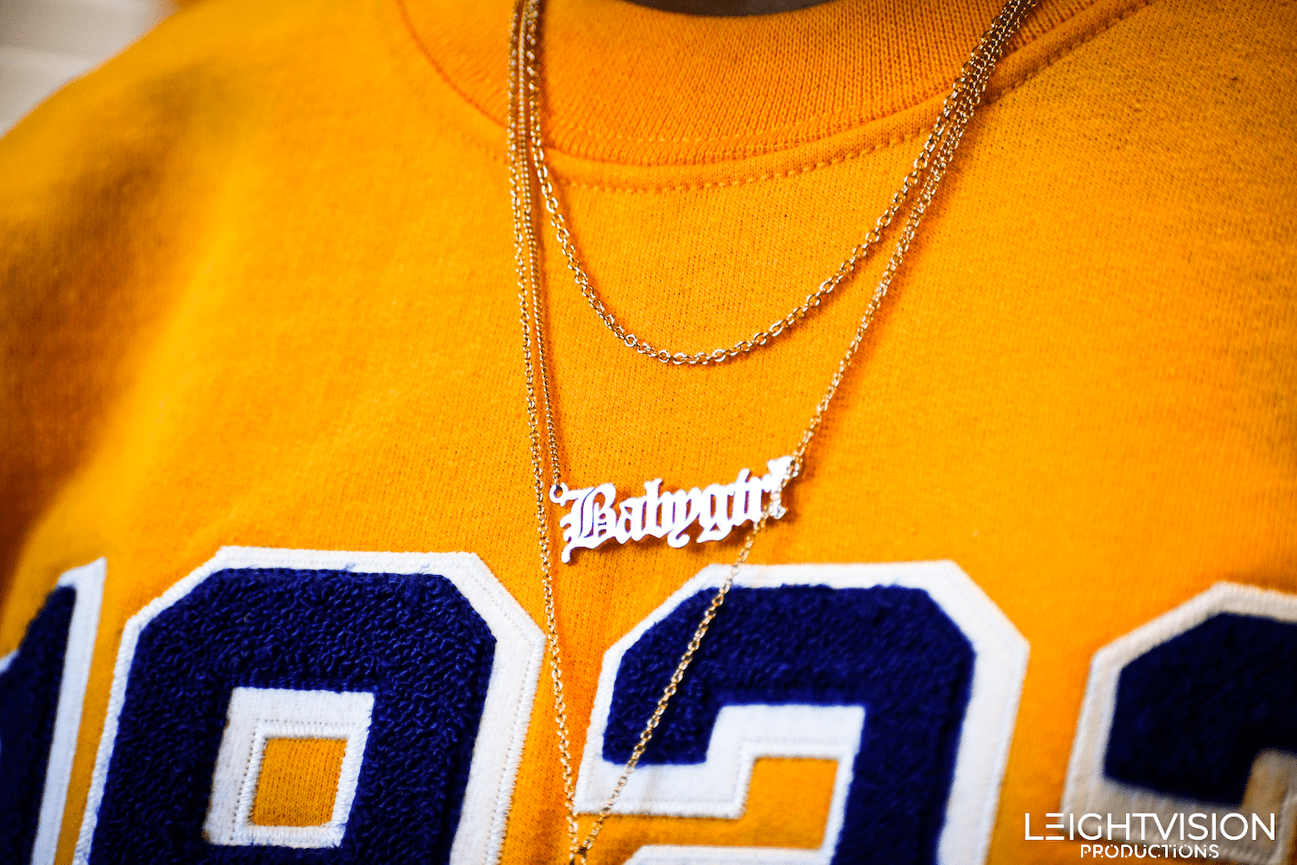 A man sporting a yellow sweatshirt and a necklace, presenting a blend of comfort and style in his attire.