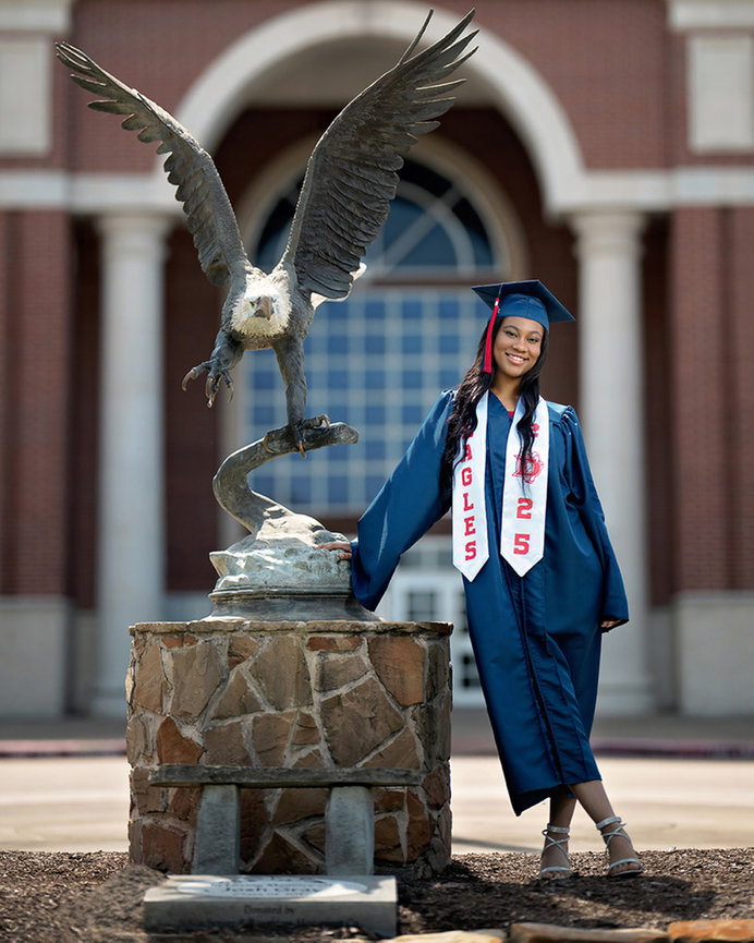 Graduate in cap and gown standing beside a stone lion statue in front of an arched building entrance