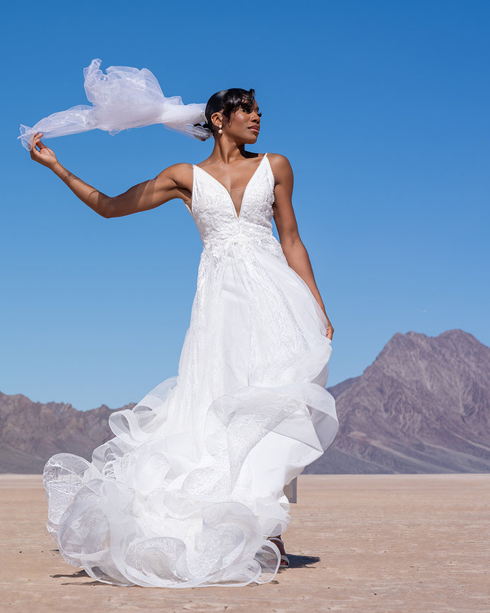 Woman in a white dress and black hat twirling in a desert landscape with mountains under a blue sky