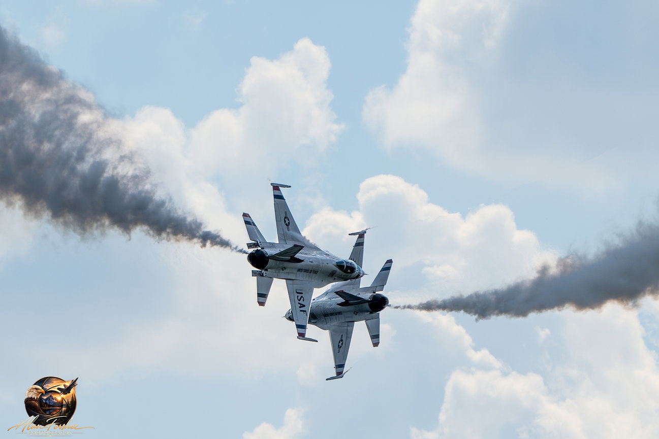 Two U.S. Air Force Thunderbirds F-16 Fighting Falcons performing a close aerial crossing maneuver with dark smoke trails.