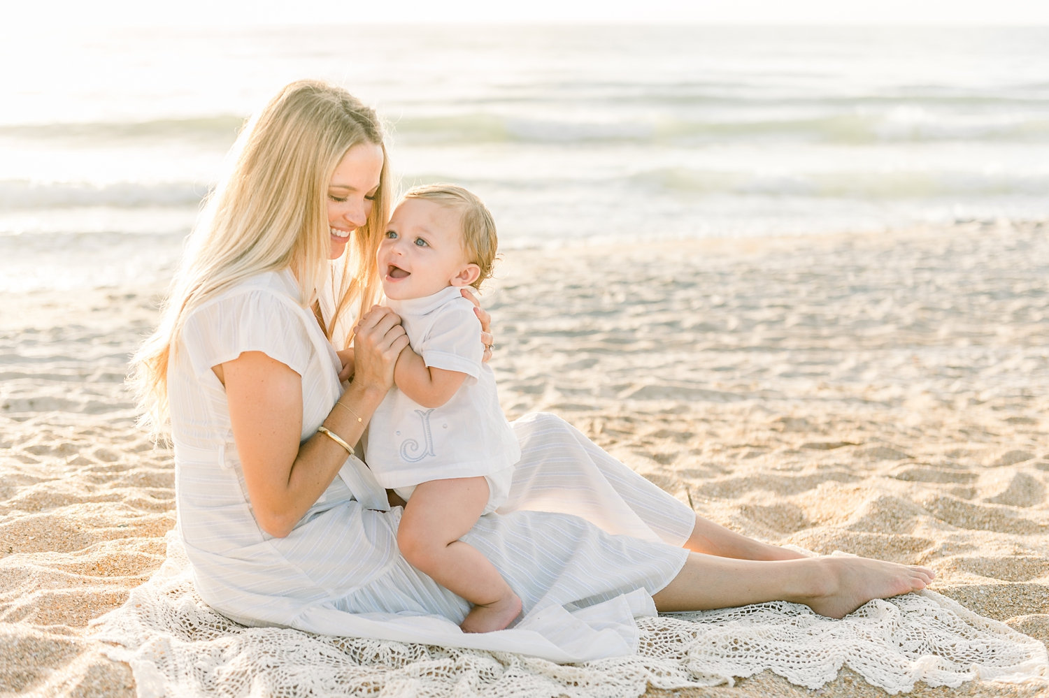 mama and baby boy laughing in the sand, mother sitting with her child in the sand